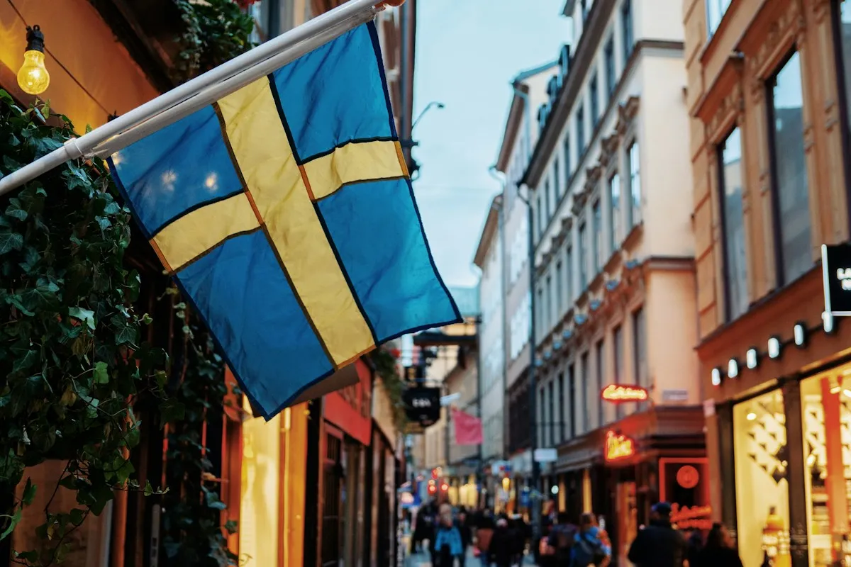 Swedish flag above a narrow shopping street in Stockholm